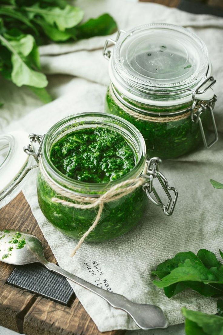 two jars filled with green pestle sitting on top of a cutting board next to a spoon