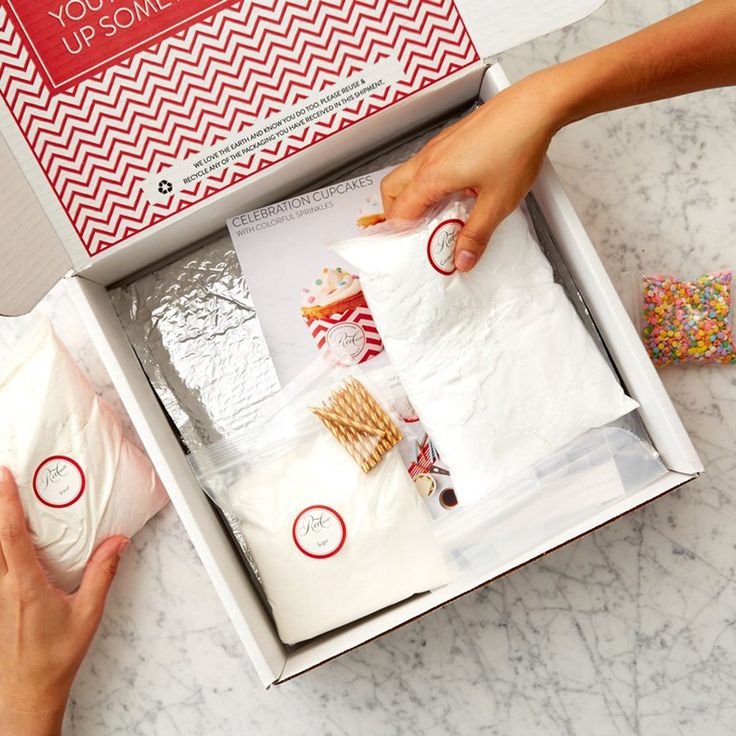 two hands reaching into an open box with sprinkles on the table next to it