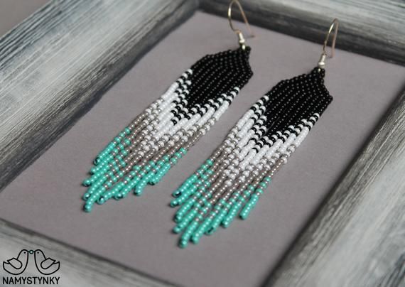 black, white and green beaded earrings with fringes on grey wood framed frame