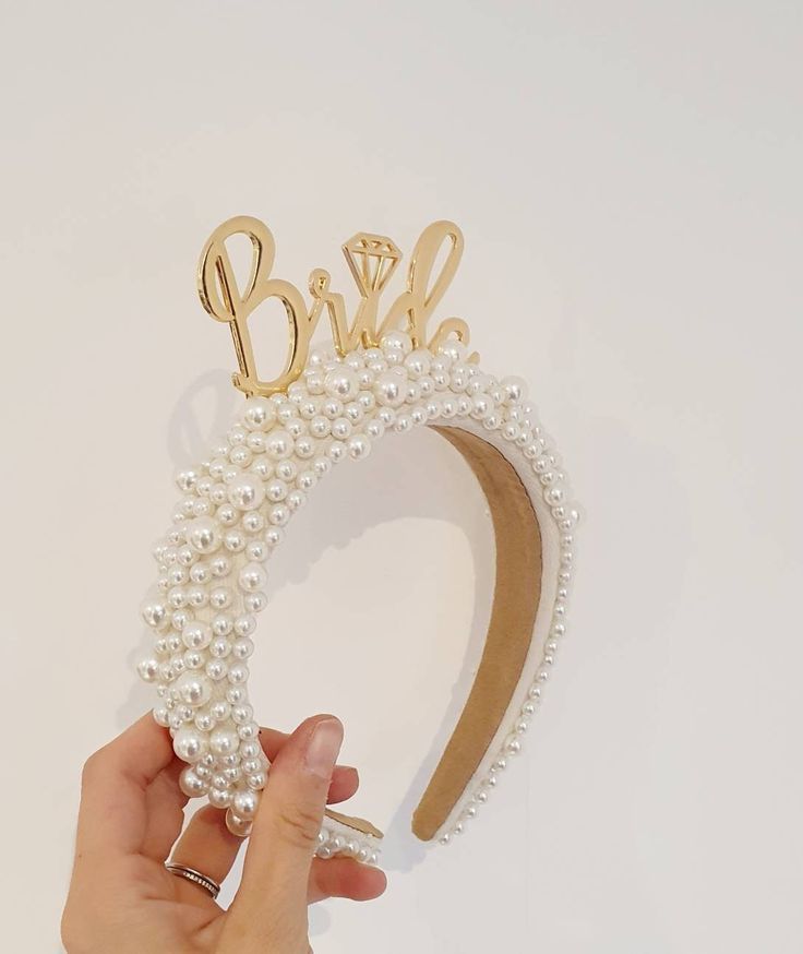 a hand holding a pearl headband with the word bride spelled in cursive letters