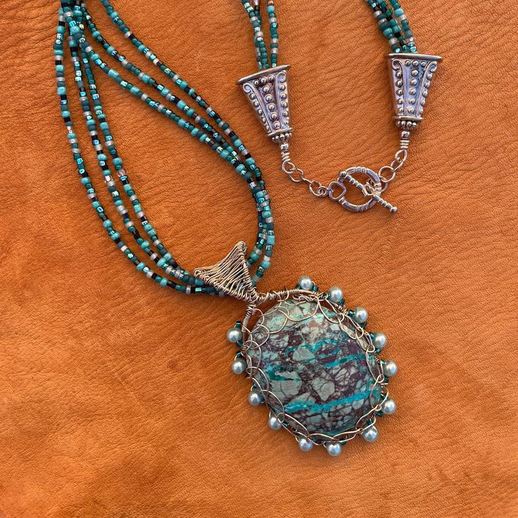 "- A handcrafted, locally sourced, one of a kind, statement necklace. - Chrysocolla is a semi-precious gemstone found in Arizona.  This one was cut and polished by a local rock hound. I bought the cabochon from him at an outdoor Boutique market in our town.  I used silver plated 20 and 26  gauge wire to weave the pendant and bail. I added 13 glass pearls around the edge of the pendant.  I used the same wire plus a small medallion on the back to secure and decorate it.    - The 21\" necklace is m Handmade Amazonite Round Beads Necklaces, Handmade Earthy Turquoise Necklace For Gift, Turquoise Jasper For Jewelry Making, Turquoise Jasper Jewelry For Jewelry Making, Unique Handmade Jasper Necklace, Artisan Amazonite Pendant Necklace, Artisan Handmade Jasper Necklaces, Elegant Handmade Turquoise Chrysocolla Necklace, Turquoise Jasper Round Bead Jewelry