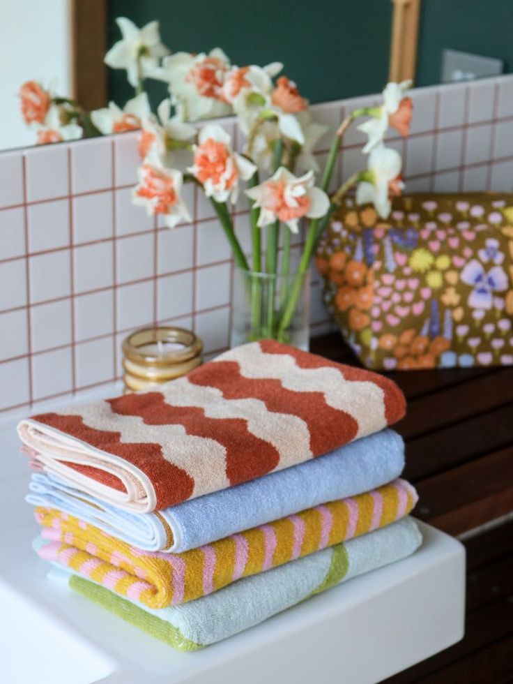 towels stacked on top of each other in front of a vase with flowers and candles