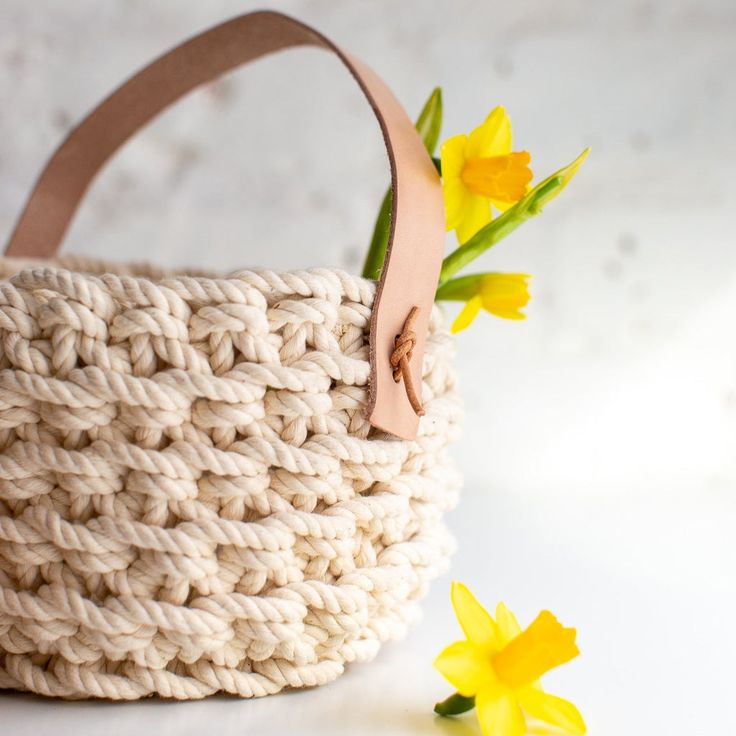 a crocheted basket with yellow flowers in front of it on a white surface