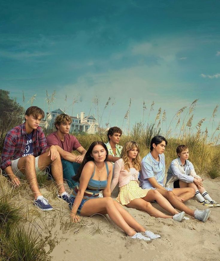 a group of young people sitting on top of a sandy beach next to tall grass