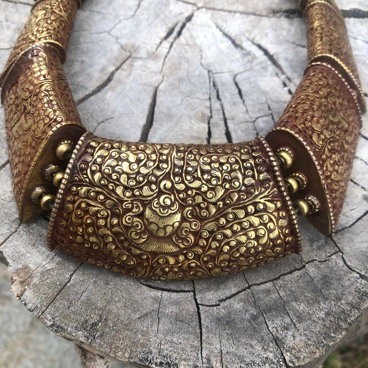 an intricately decorated bracelet sitting on top of a piece of wood next to a tree stump