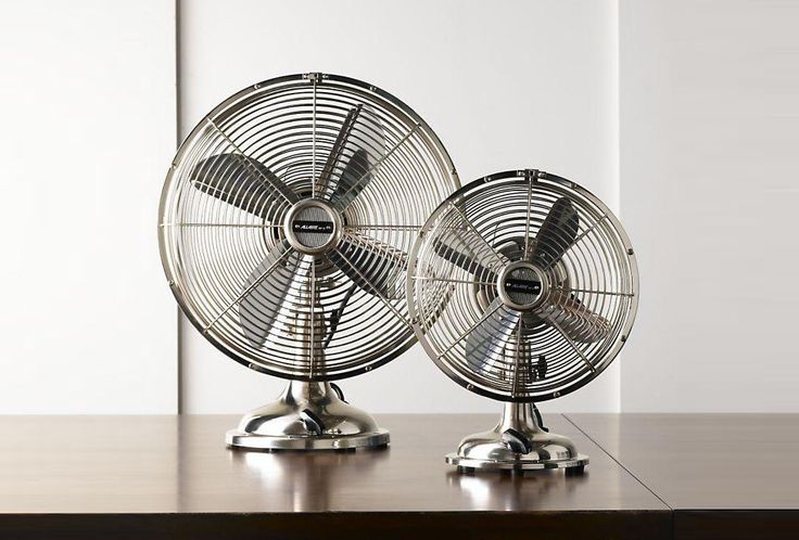 two metal fans sitting on top of a wooden table