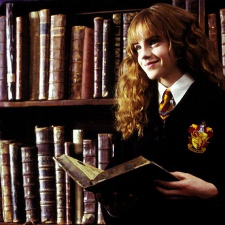 a woman in a harry potter costume holding a book and smiling at the camera while standing in front of bookshelves