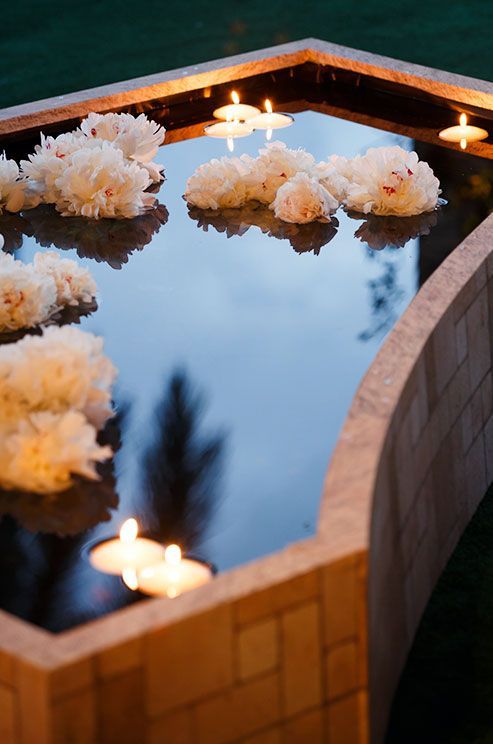 flowers and candles are placed on the surface of a pond that is surrounded by bricks