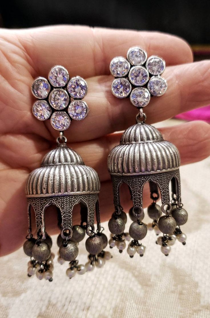 Gather compliments wearing this Indian jhumka earrings with flashy CZ ear studs. In faux diamond, ruby, emerald, and blue sapphire. Voluptuous shape. Very feminine and pretty! Tiny dangly metal balls and pearls finish the look. Earrings are cast metal, not stamped, so they look and feel substantial. find even more great earrings here: https://www.etsy.com/shop/boutiquebymaryam?section_id=22797814 Be sure to visit the rest of my shop here: https://www.etsy.com/shop/boutiquebymaryam All my jewelry Silver Pearl Earrings With Stone Work For Celebration, Temple Jewelry Jhumkas As A Gift, Temple Jewelry Style Jhumkas For Anniversary, Gift Temple Jewelry Jhumkas, Gift Stone Work Pearl Drop Earrings, Hand Set Silver Jhumkas For Festive Occasions, Silver Hand-set Jhumkas For Festive Occasion, Fusion Style Dangle Jhumkas For Wedding, Silver Chandelier Earrings With Stone Work For Festivals