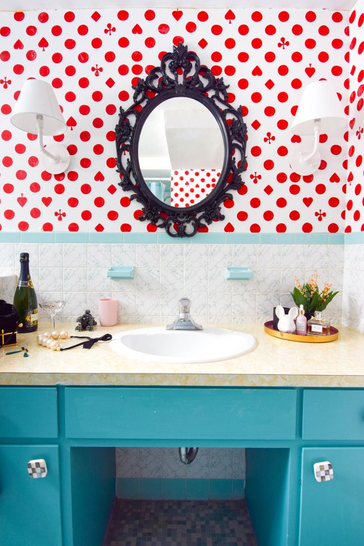 a bathroom with blue cabinets and red polka dot wallpaper on the walls, along with a round mirror