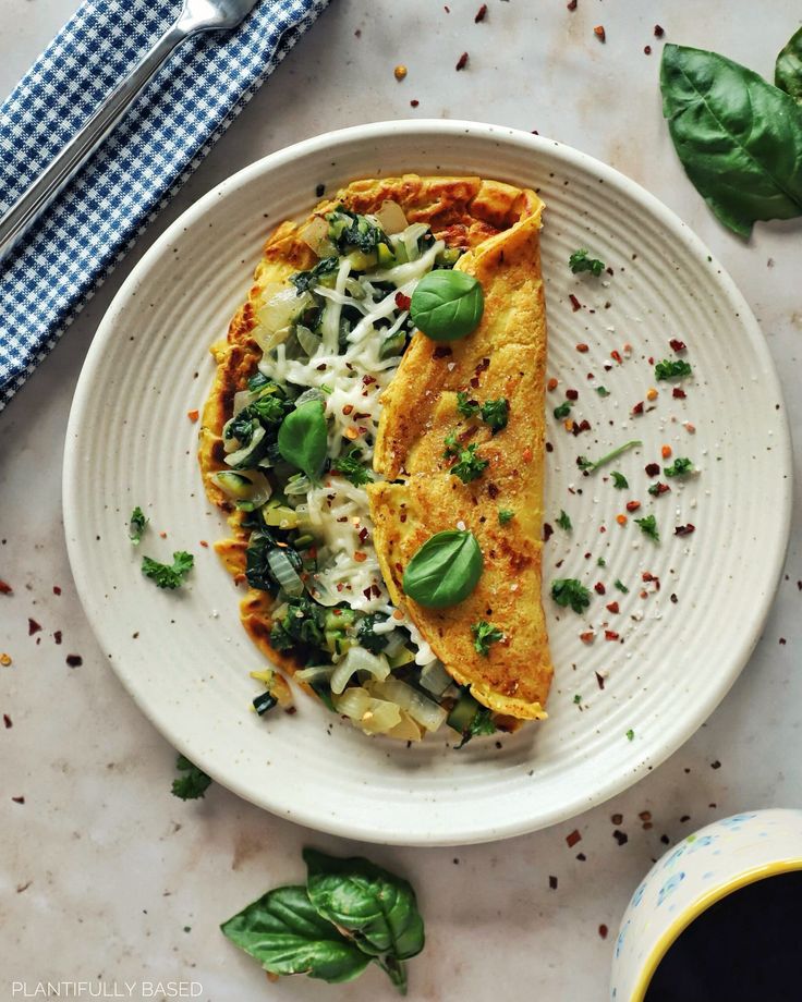 a white plate topped with an omelet covered in cheese and spinach next to a cup of coffee