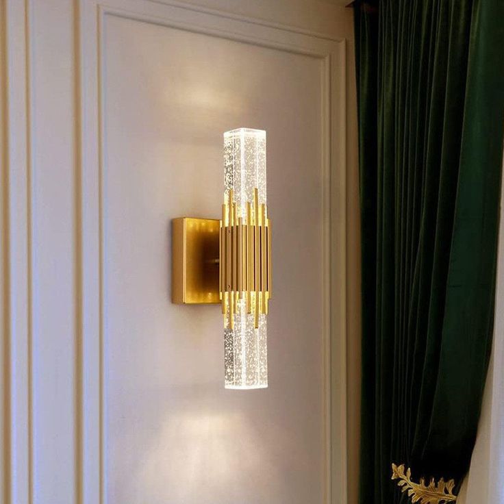 a wall mounted light on the side of a white door with green curtains behind it