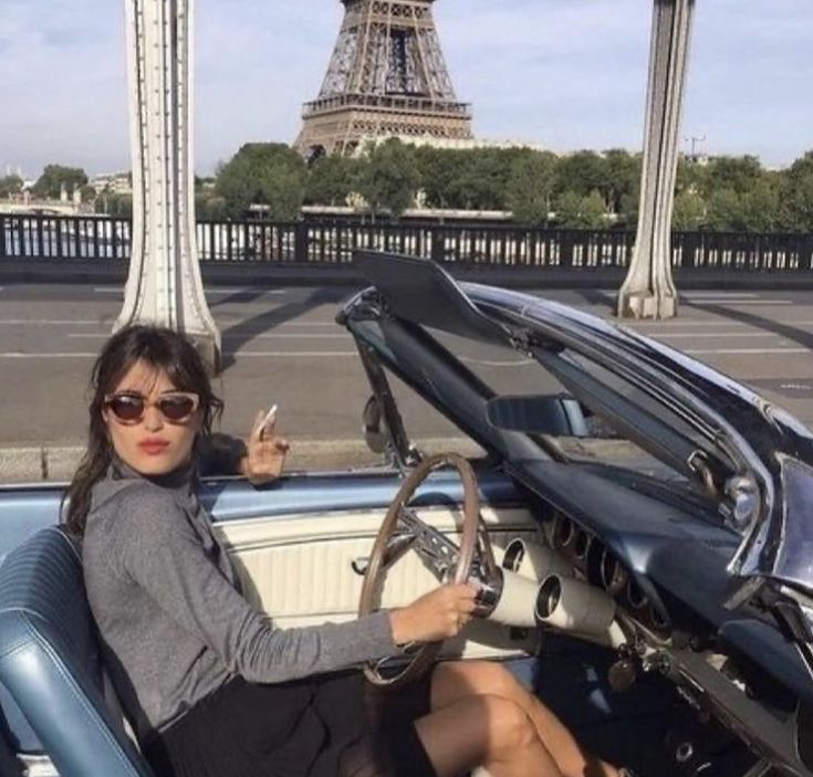 a woman sitting in the driver's seat of a car with the eiffel tower in the background