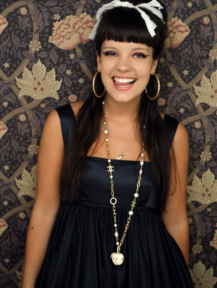 a young woman wearing a black dress with a white flower in her hair smiling at the camera