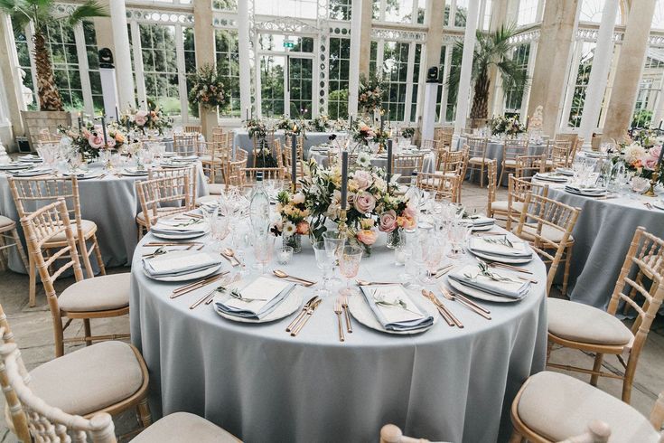 a table set up for a formal dinner in a glass walled dining room with large windows