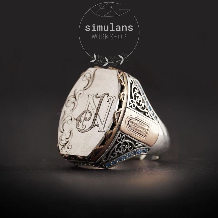 This handcrafted sterling silver men's ring features a unique customizable initials design, perfect for adding a personal touch. The ring is made from high-quality 925 sterling silver and is adorned with intricate engravings. The center showcases a monogram design, as shown with "N J" initials, but can be personalized with any initials, name, or logo of your choice. The sides of the ring are embellished with a bronze door motif and surrounded by blue micro zircon stones, adding a touch of elegan Luxury Silver Initial Ring, Luxury Silver Initial Ring Hallmarked, Luxury Silver Initial Ring For Wedding, Luxury Silver Hallmarked Initial Ring, Silver Monogram Engraved Ring For Wedding, Formal Silver Rings With Initials, Formal Silver Monogram Rings, Silver Wedding Ring With Engraved Initials, Silver Sterling Signet Ring With Initials