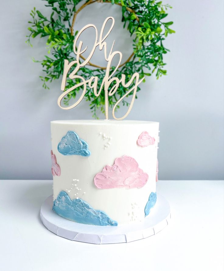 a white cake with pink and blue frosting on top that says oh baby next to a wreath