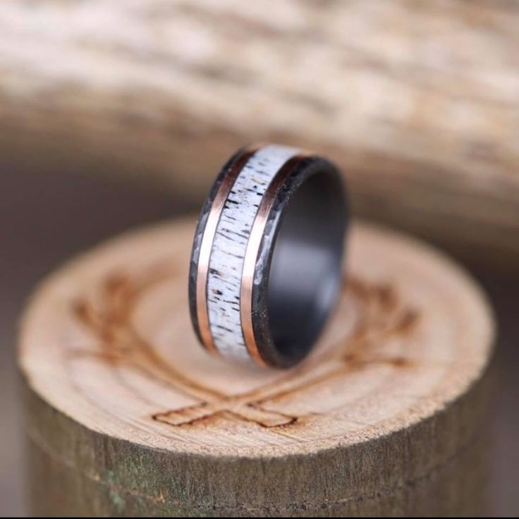 a wedding ring that is sitting on top of a piece of wood with silver and black inlays