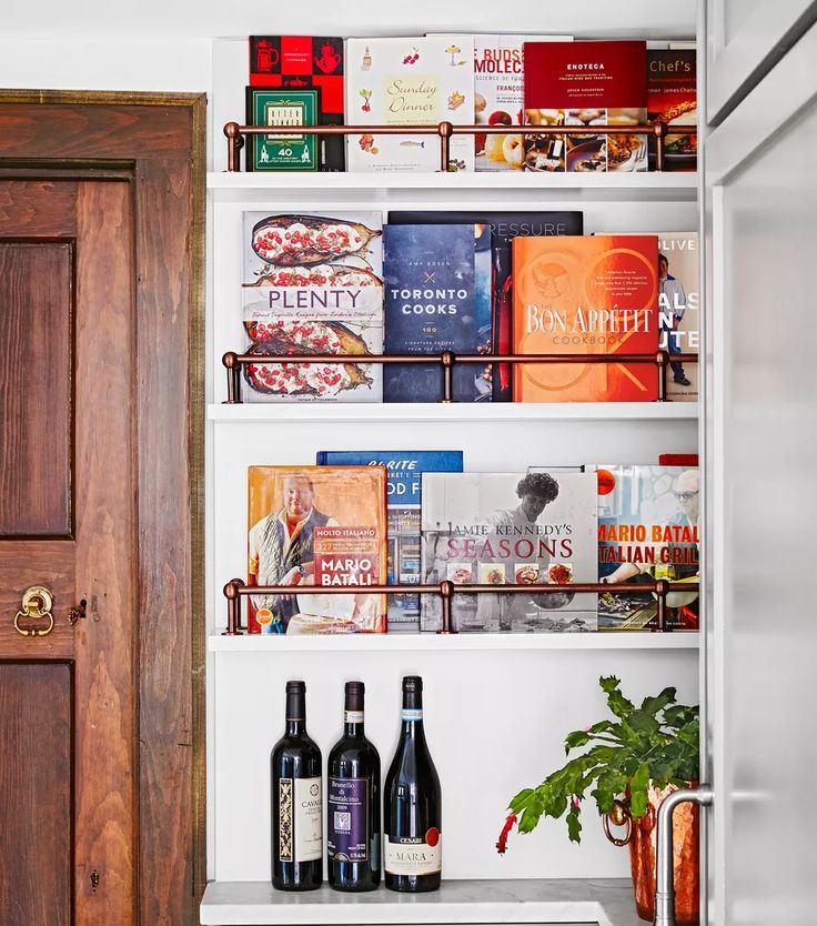 an open pantry with wine bottles and books on the shelves next to a wooden door