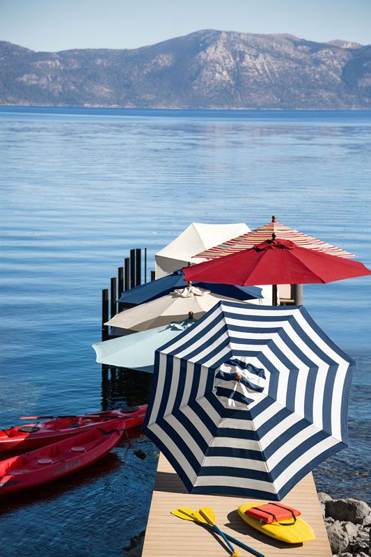 several umbrellas and kayaks are on the dock by the water's edge