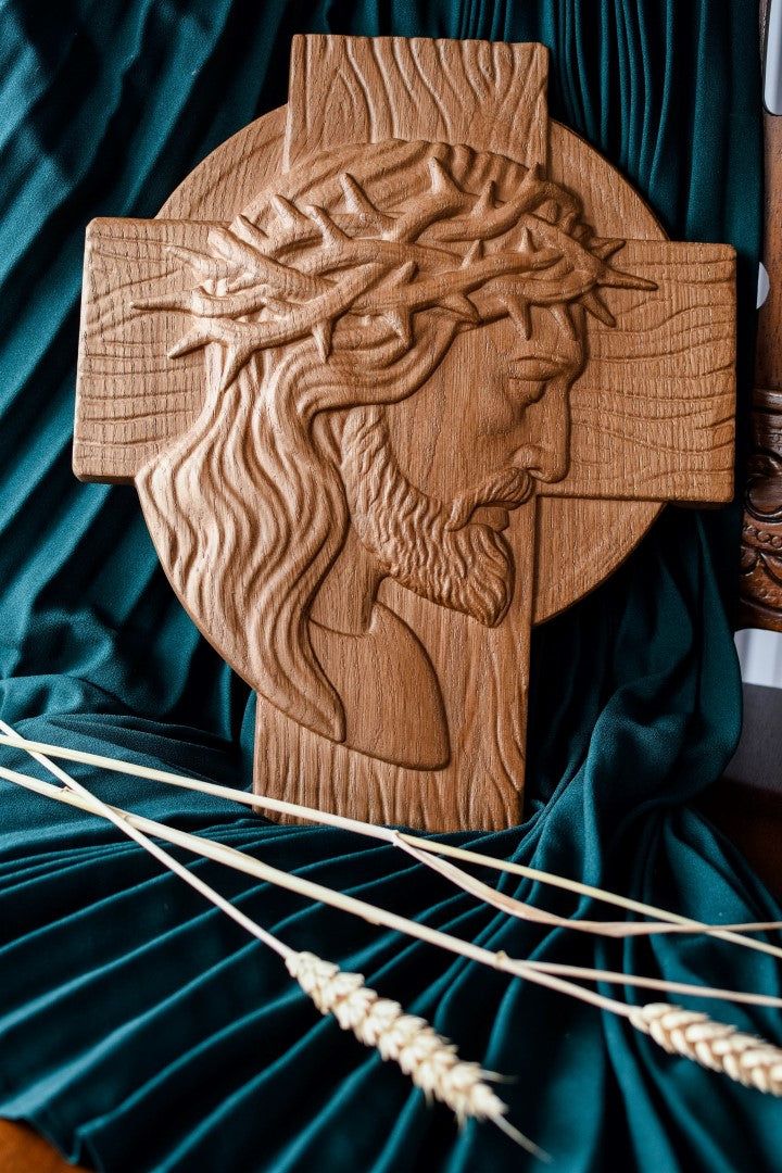 a wooden cross with the image of jesus on it and wheat stalks in front of it