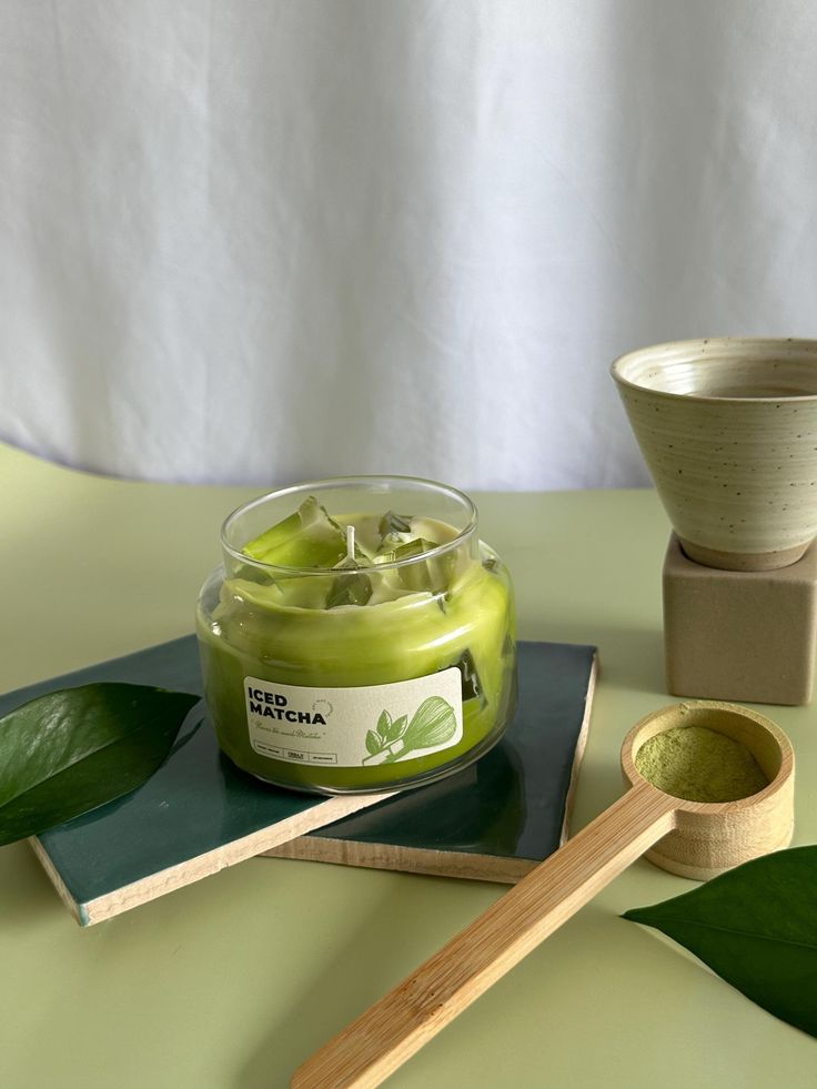 a jar of green tea sits on a table next to two wooden spoons