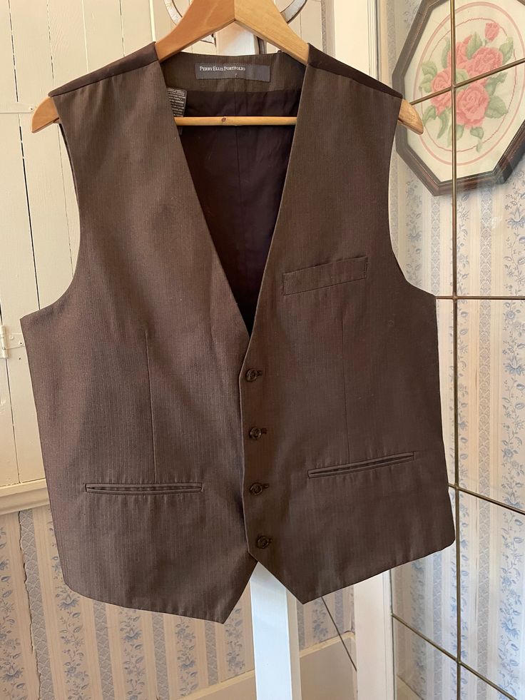 This classic tailored vest by Perry Ellis Portfolio is made from a medium weight blend of 70 per cent polyester and 30 per cent cotton in dark brown with a very fine black pattern. It has the original buttons in the front and three front pockets. The back and lining are made from a dark brown polyester cotton blend. Marked size large. The measurements, taken with the vest lying flat, are: shoulder to shoulder, 15 inches; armpit to armpit, 22 inches; length, 26 inches in front and 23 inches in back; bottom edge, 23 inches. In very good condition. Business Vest With Welt Pockets For Fall, Brown Sleeveless Formal Outerwear, Formal Brown Sleeveless Outerwear, Semi-formal Sleeveless Vest With Pockets, Brown Business Vest For Fall, Business Vest For Fall, Sleeveless, Fall Business Vest Sleeveless, Fitted Brown Vest For Semi-formal Occasions, Brown Fitted Vest For Semi-formal Occasions