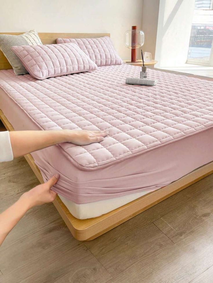 a person reaching for a pink mattress on a wooden bed frame in a room with hardwood floors