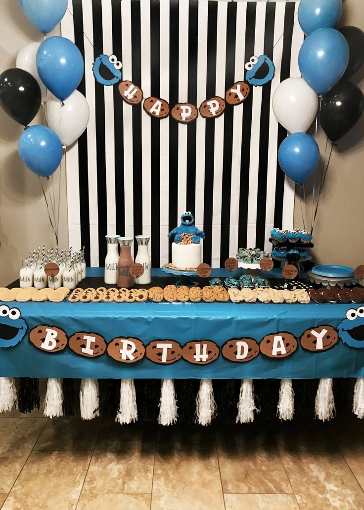 a blue table topped with cookies and cupcakes next to black and white balloons