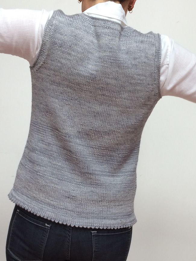 a woman with her back turned to the camera wearing a gray sweater vest and black jeans