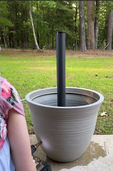 a woman sitting on the ground in front of a large bowl with a black stick sticking out of it