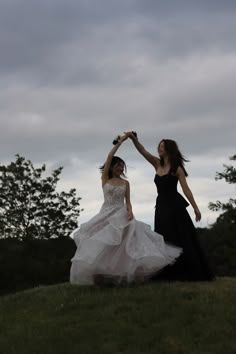 two women in black dresses are dancing on a hill with their arms around each other