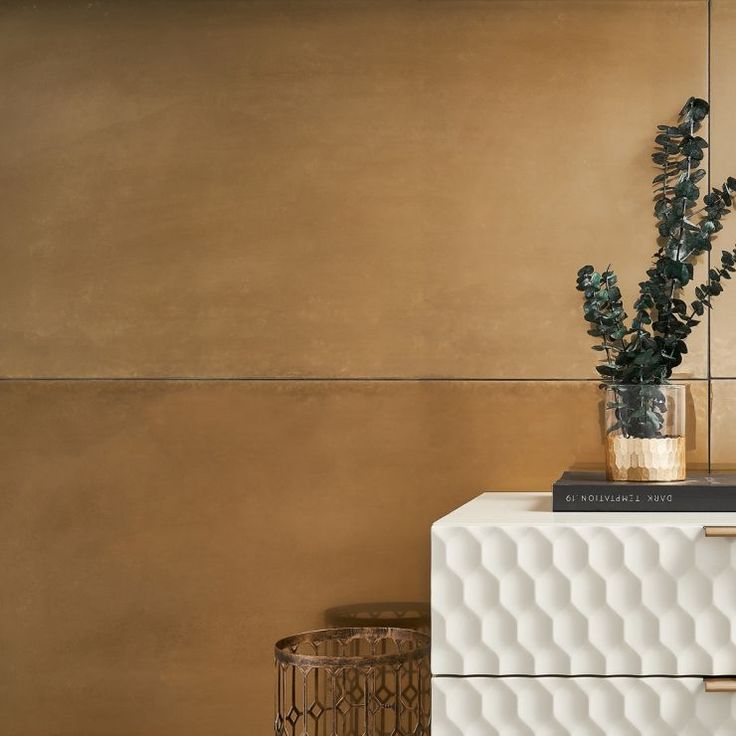 a vase with some plants on top of a white cabinet next to a gold wall