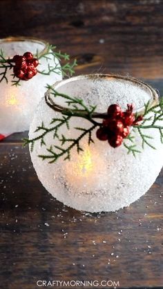 two snow globes with red berries and greenery on them sitting on a wooden table