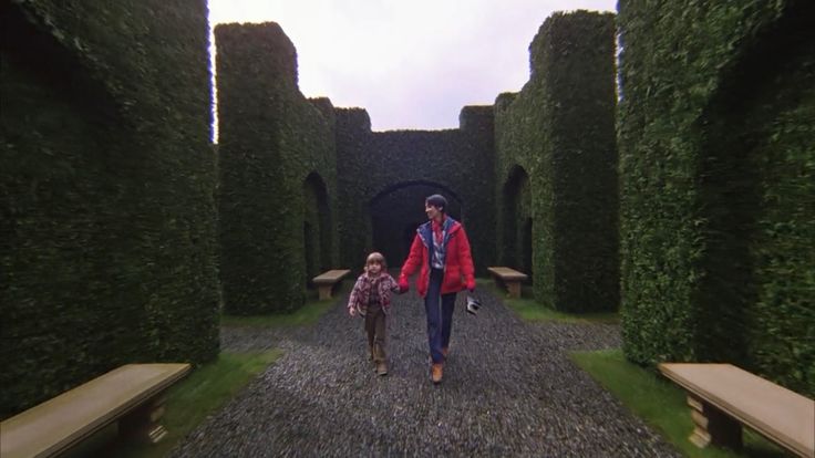 a woman and child are walking through an archway in the middle of a garden area