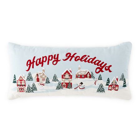 a pillow with the words happy holidays written in red and white on it, surrounded by snow covered houses