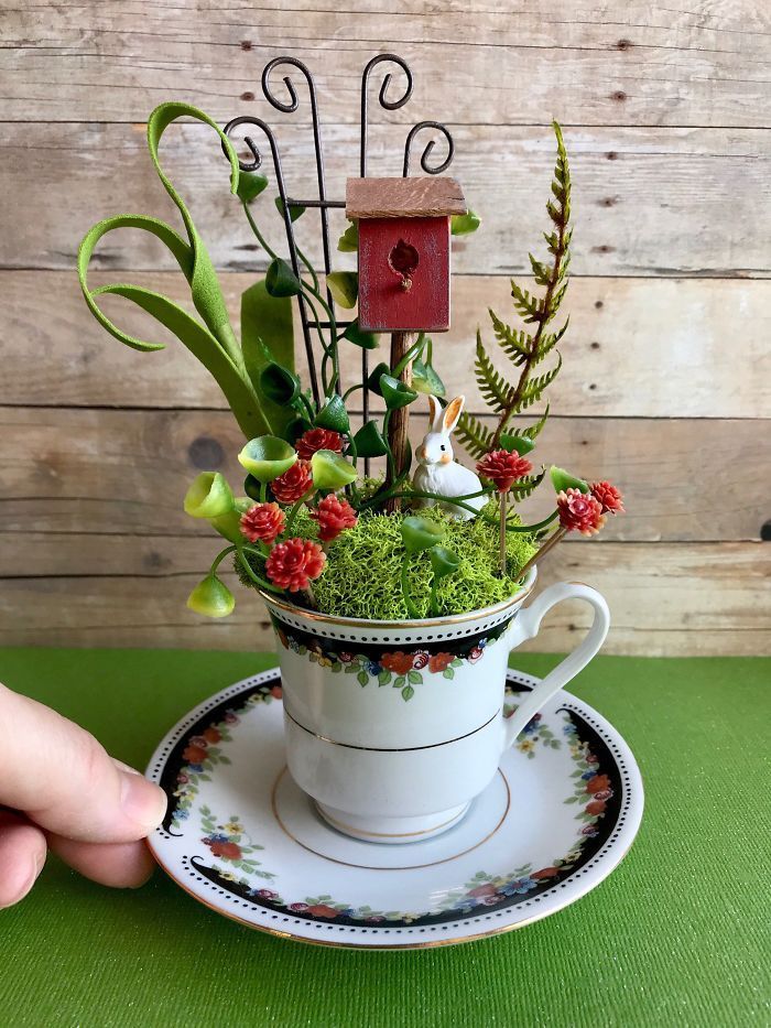 a cup filled with plants sitting on top of a saucer next to a birdhouse