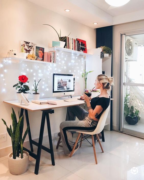 a woman sitting at a desk in front of a computer monitor with lights on the wall behind her