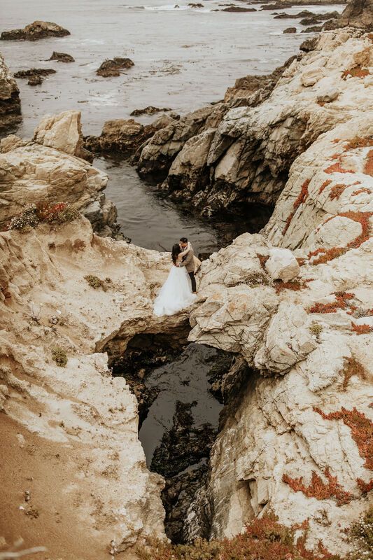 a bride and groom standing on rocks near the ocean