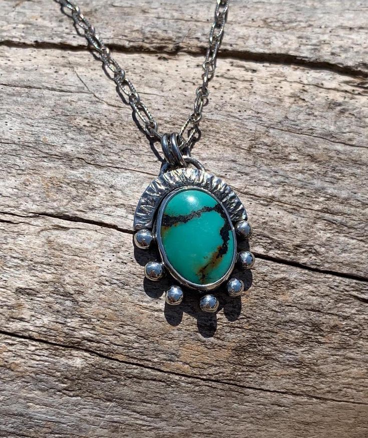 This oval Turquoise is set within a fine silver bezel, and surrounded and backed with sterling silver. Two lines of black and golden brown matrix run through the turquoise field like little trails.  Seven silver orbs adorn the bottom two-thirds of the setting. The remaining third is protected by a hammered and notched arcing sterling wall. The entire necklace has been oxidized and polished to enhance the details of the design. The chain is a textured long and short style and has been finished wi Artisan Sterling Silver Turquoise Necklace, Turquoise Cabochon Chrysocolla Necklace, Handmade Artisan Turquoise Oval Necklace, Handmade Artisan Oval Turquoise Necklace, Artisan Handmade Oval Turquoise Necklace, Oval Turquoise Natural Stone Necklaces, Sterling Silver Turquoise Necklace With Oxidized Finish, Artisan Turquoise Oval Necklace, Turquoise Oval Natural Stones Necklaces