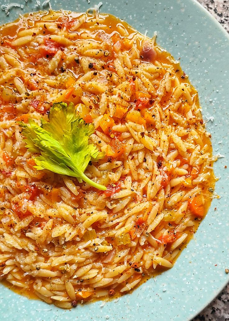 a blue plate topped with pasta covered in sauce and garnished with a green leaf