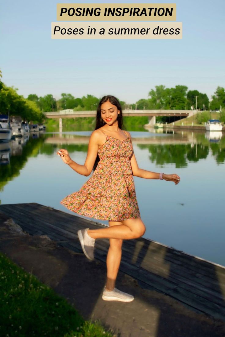 a woman in a dress is posing on a dock by the water with her arms spread out