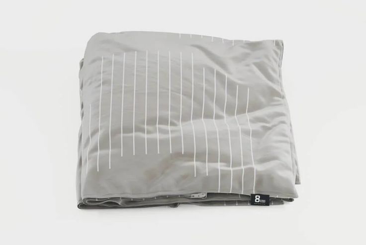 a gray and white blanket laying on top of a bed next to a black pillow