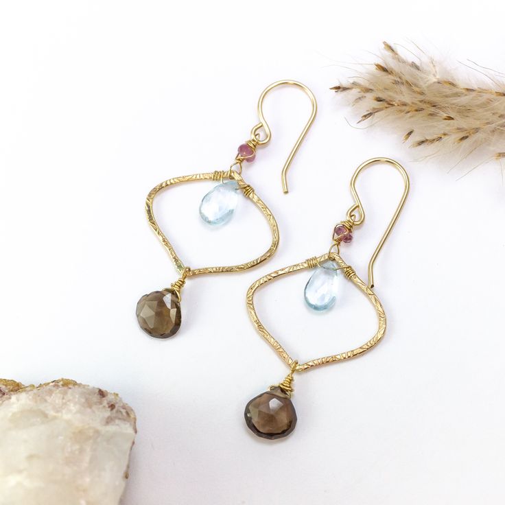 Immerse yourself in the whimsical charm of our Boho Aurora Earrings. These earrings are a celebration of bohemian elegance and the radiant palette of autumn's dawn. Handcrafted with care, each earring boasts unique handmade and textured components that reflect the individuality found in the natural world. Delicate wire-wrapped pink tourmaline gems crown the top, adding a touch of delicate femininity that's reminiscent of the season's blossoms. Inside the components, nestled like secrets waiting Aurora Earrings, Smoky Topaz, Jewelry Design Inspiration, The Natural World, Boho Luxe, Jewelry Repair, Topaz Gemstone, Pink Tourmaline, Natural World