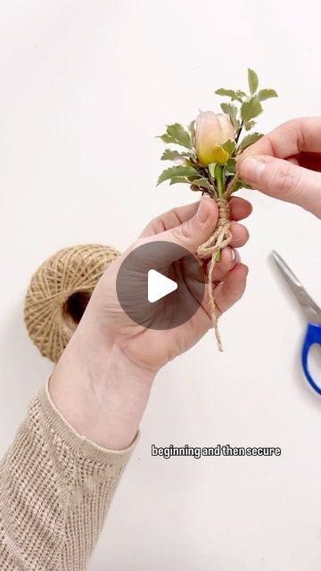 someone is holding a flower in their hand with scissors and yarn on the table next to it