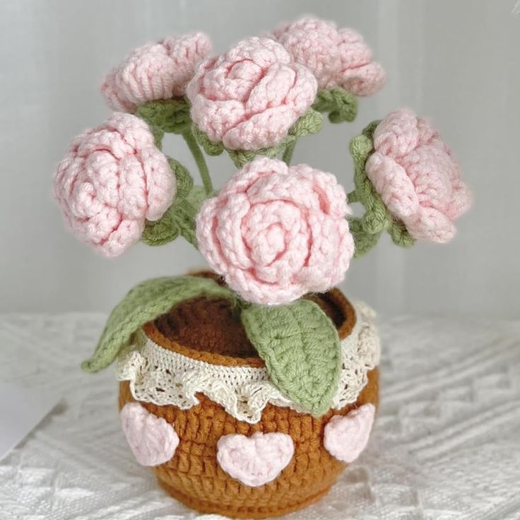 a crocheted vase with pink flowers in it on a white tableclothed surface