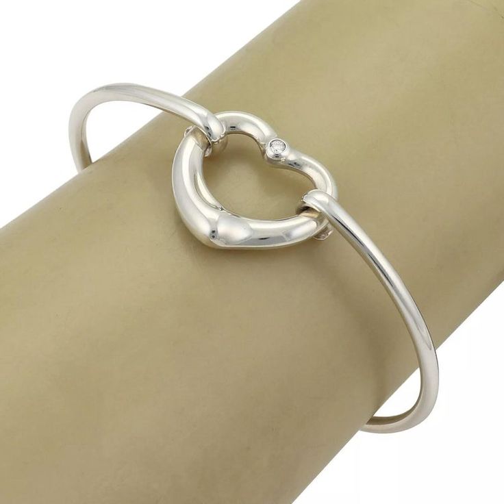 Material: sterling silver Hallmark: Tiffany & Co. Peretti 925 Spain Measurement: inner circumference: 6.5" x 0.10" thick Heart: 0.77" tall x 0.84" wide x 0.16" thick Weight: 13.4 grams  This authentic bangle is from Tiffany & Co. by designer Elsa Peretti from her Open Heart collection. It is crafted from sterling silver with a 2.5mm thick wire bangle, the front has the contour open heart with a 2 points diamond at the top of the heart. One end of the bangle has a small curved hook which and secu Modern Sterling Silver Jewelry For Valentine's Day, Luxury Sterling Silver Heart Bracelet For Anniversary, Luxury Sterling Silver Bracelets For Valentine's Day, Silver Bracelets For Valentine's Day Formal Occasion, Silver Bracelets For Valentine's Day Formal Event, Valentine's Day Silver Bracelet For Formal Occasions, Sterling Silver Heart-shaped Bracelet In White Gold For Anniversary, Sterling Silver Bangle With Heart Charm, Anniversary Sterling Silver Bangle With Silver Clasp