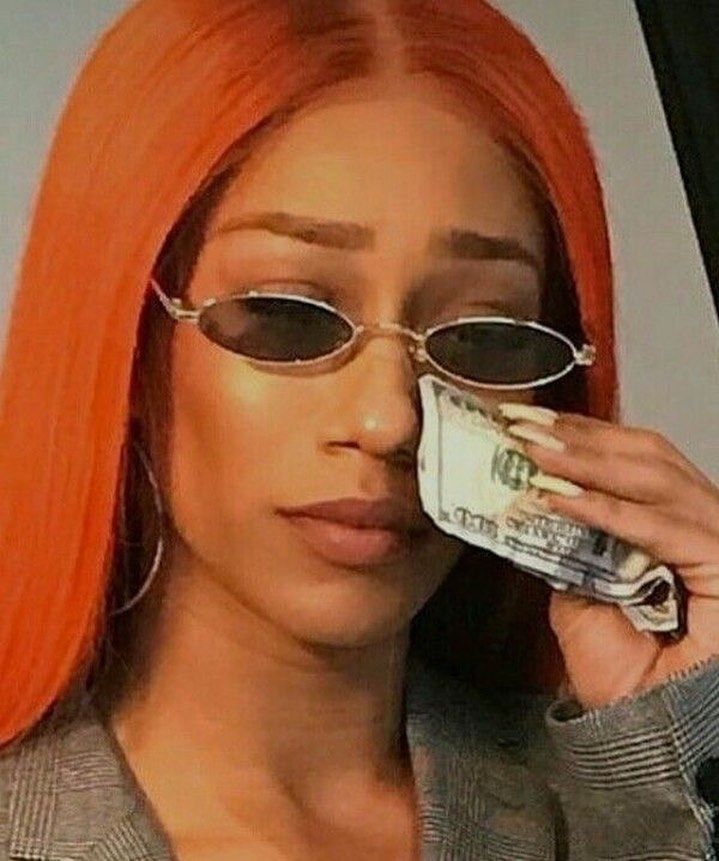 a woman with orange hair and sunglasses talking on a cell phone while holding money in her hand