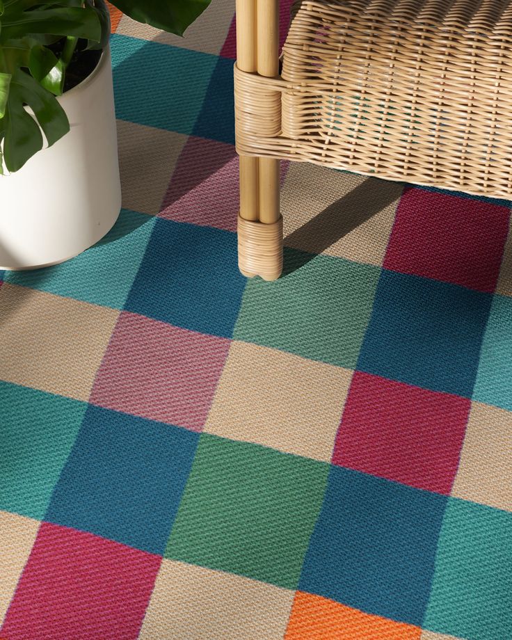 a chair and potted plant sitting on a checkered rug in front of a wicker bench