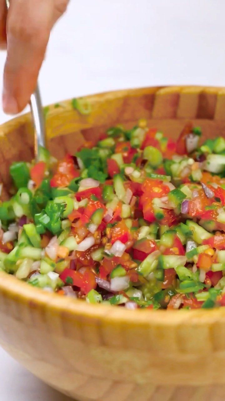 a wooden bowl filled with lots of veggies on top of a white table